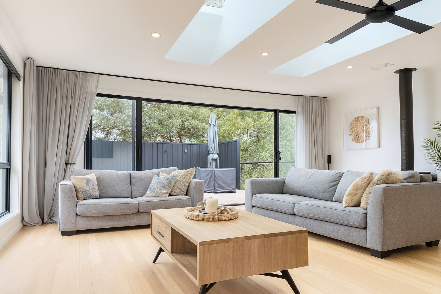A modern living room with two grey sofas, a wooden coffee table, and large windows with curtains.