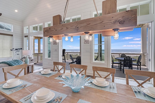 A dining area with a wooden table set for four, large windows, and a view of the ocean.