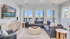 A modern living room with a large TV, comfortable seating, a wooden console, and large windows offering a view of the outdoors.