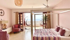 A bedroom with a bed, a chair, a desk, a lamp, and a view of the ocean.