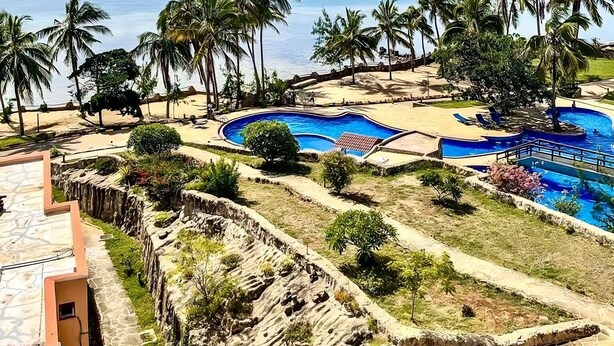 A resort with a large pool area, palm trees, and a view of the ocean.