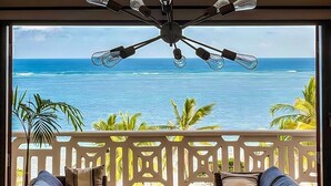 A room with a ceiling fan, a view of the ocean, and two wicker sofas with cushions.