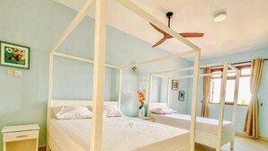 A bedroom with a four-poster bed, two bedside tables, a nightstand, a ceiling fan, and a window with curtains.