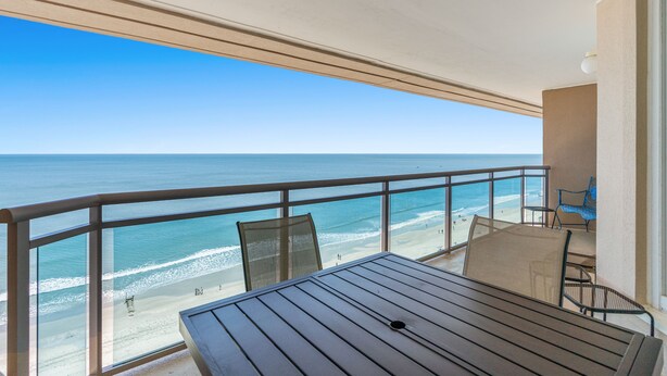 Un balcon avec une table et des chaises donnant sur une plage.