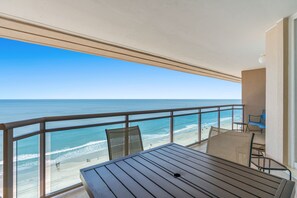 Ein Balkon mit Tisch und Stühlen mit Blick auf einen Strand.