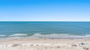Une plage avec un ciel dégagé, une eau calme et des gens qui se détendent sur le sable.