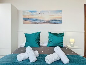 A hotel room with a bed featuring teal pillows, a view of the sea with birds, and a lamp on the nightstand. - Casa Moreira by Atlantic Holiday (Machico)