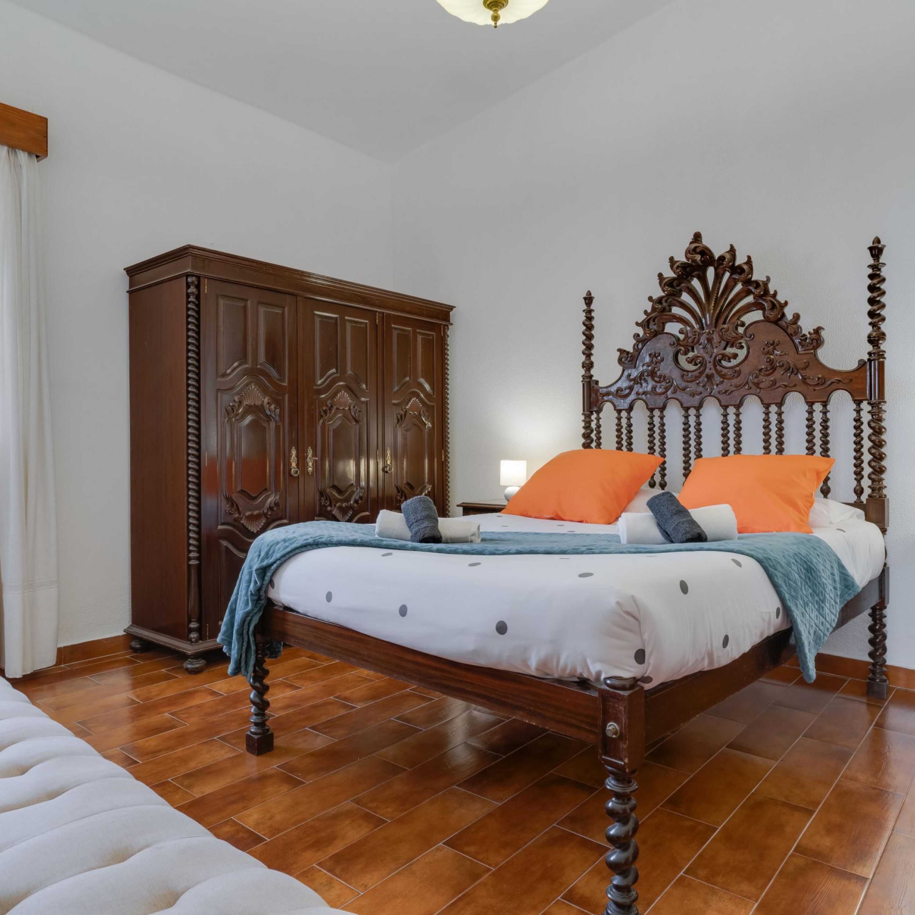 Une chambre à coucher avec un lit en bois, une armoire et un sol carrelé.
