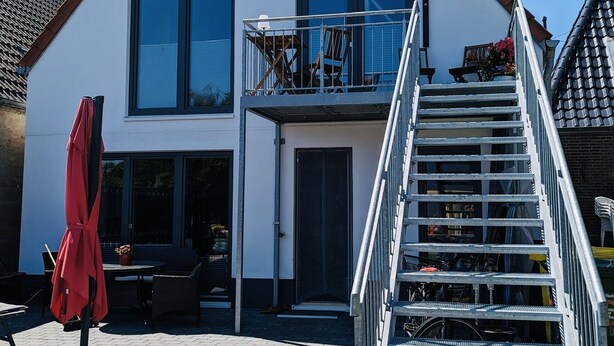 A two-story house with a balcony, a staircase, and a patio area with outdoor furniture. - 2 Bedroom Apartment in Bredstedt (Bredstedt)