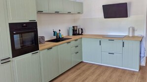 A modern kitchen with light green cabinets, a black oven, a wooden countertop, and a flat-screen TV mounted on the wall. - 2 Bedroom Apartment in Bredstedt (Bredstedt)