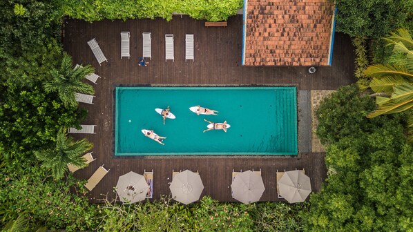 An aerial view of a swimming pool surrounded by wooden deck, lounge chairs, and umbrellas. - We Escape (Weligama)