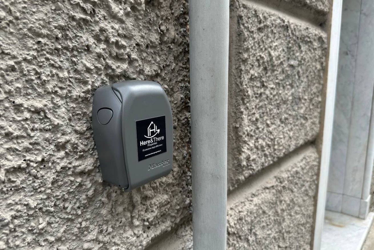 Ein graues, rechteckiges Gerät, das an einer strukturierten Wand angebracht ist und ein Logo sowie Text enthält.
