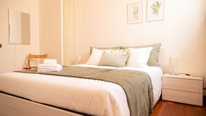 A neatly made bed with a green blanket, a bedside table with a lamp, and a wall-mounted mirror. - [Luxury Savona] Cruises 1 min • Free WiFi • A/C (Savona)