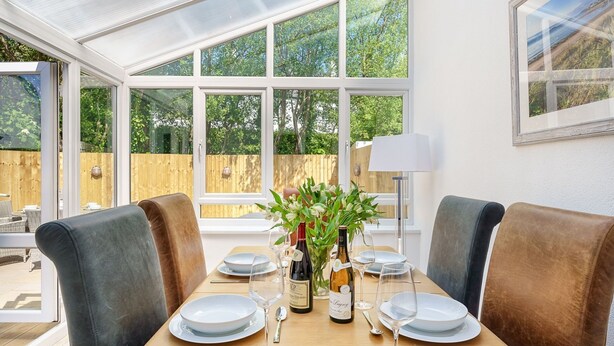 Un comedor con una mesa dispuesta para cuatro personas, rodeada de sillas acolchadas, y vista a una valla de madera y follaje al exterior.