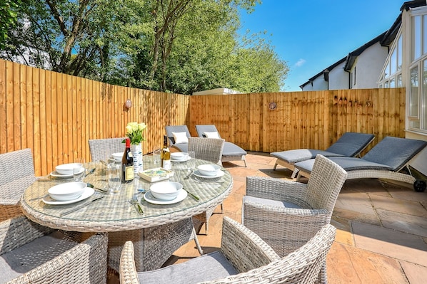 A round glass table with white plates and cutlery, surrounded by wicker chairs and a wicker sofa.