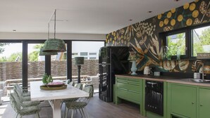 Una cocina moderna con armarios verdes, un comedor con mesa y sillas blancas, y un ventanal con vistas al exterior.