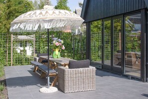 An outdoor patio with a table and chairs, a wicker sofa, a decorative umbrella, and a vase with flowers.