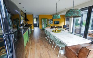 A modern kitchen with a long dining table, green chairs, and a large window.