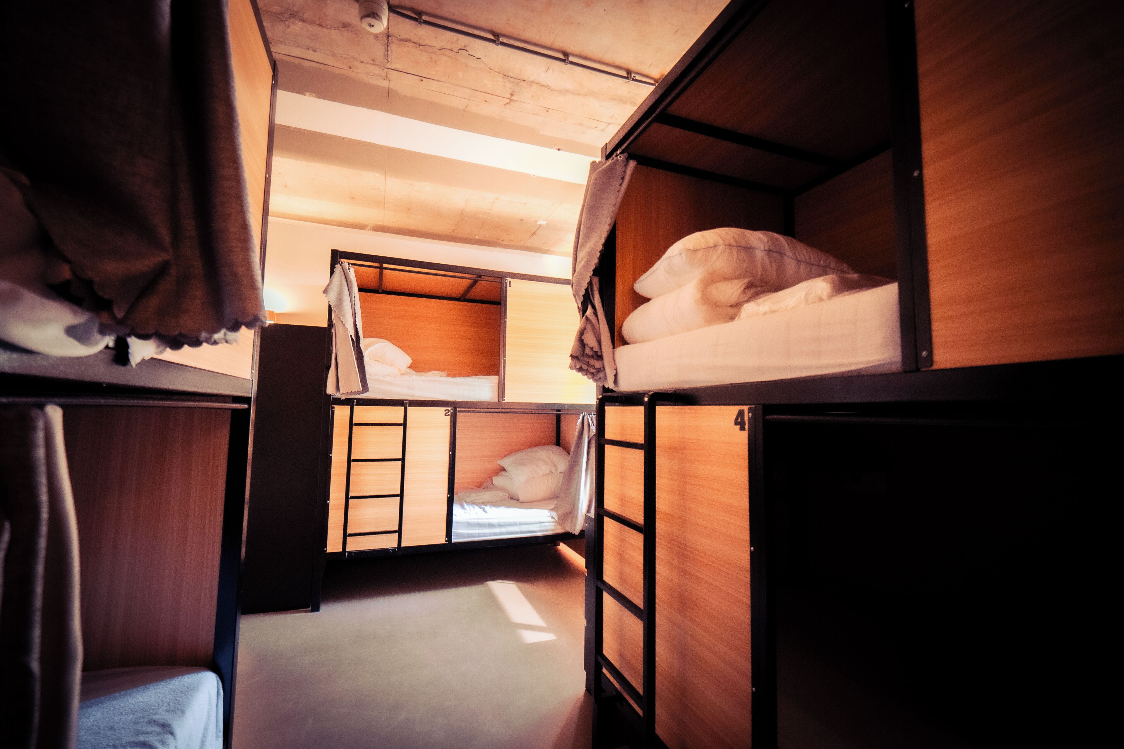 A compact, multi-bed RV interior with wooden walls and a slanted ceiling, featuring bunk beds and a small seating area.