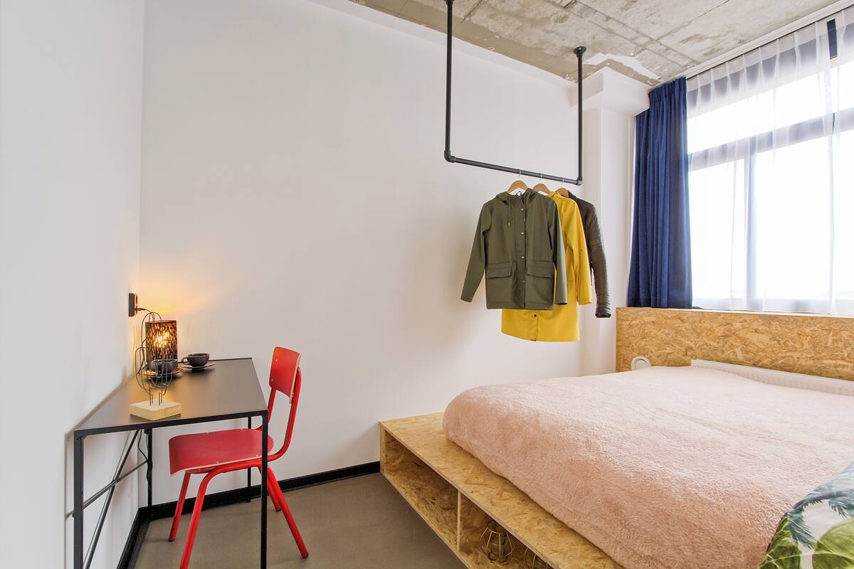 Une chambre à coucher comprenant un lit, un bureau, une chaise et un porte-manteau mural.