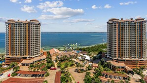 A high-rise hotel with a view of the ocean, featuring multiple balconies, a parking area, and a beachside resort.