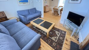 A living room with a blue sofa, a glass coffee table, and a TV on a stand. - 37 Trenwith Place - a cottage that sleeps 5 guests in 3 bedrooms (St Ives)
