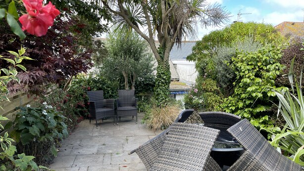 A patio with wicker furniture, a stone pathway, and lush greenery. - 37 Trenwith Place - a cottage that sleeps 5 guests in 3 bedrooms (St Ives)