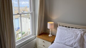 A bedroom with a window, a bedside table with a lamp, and a bed with white bedding. - 37 Trenwith Place - a cottage that sleeps 5 guests in 3 bedrooms (St Ives)