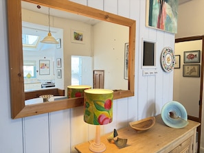 A wooden-framed mirror reflecting a kitchen with a stove, a hanging pendant light, and a window.