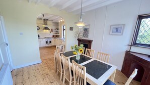 A dining area with a table and chairs, a hanging light fixture, and a view into the kitchen. - Stratton Vow - a true 1920s Arts and Crafts house! (St Ives)