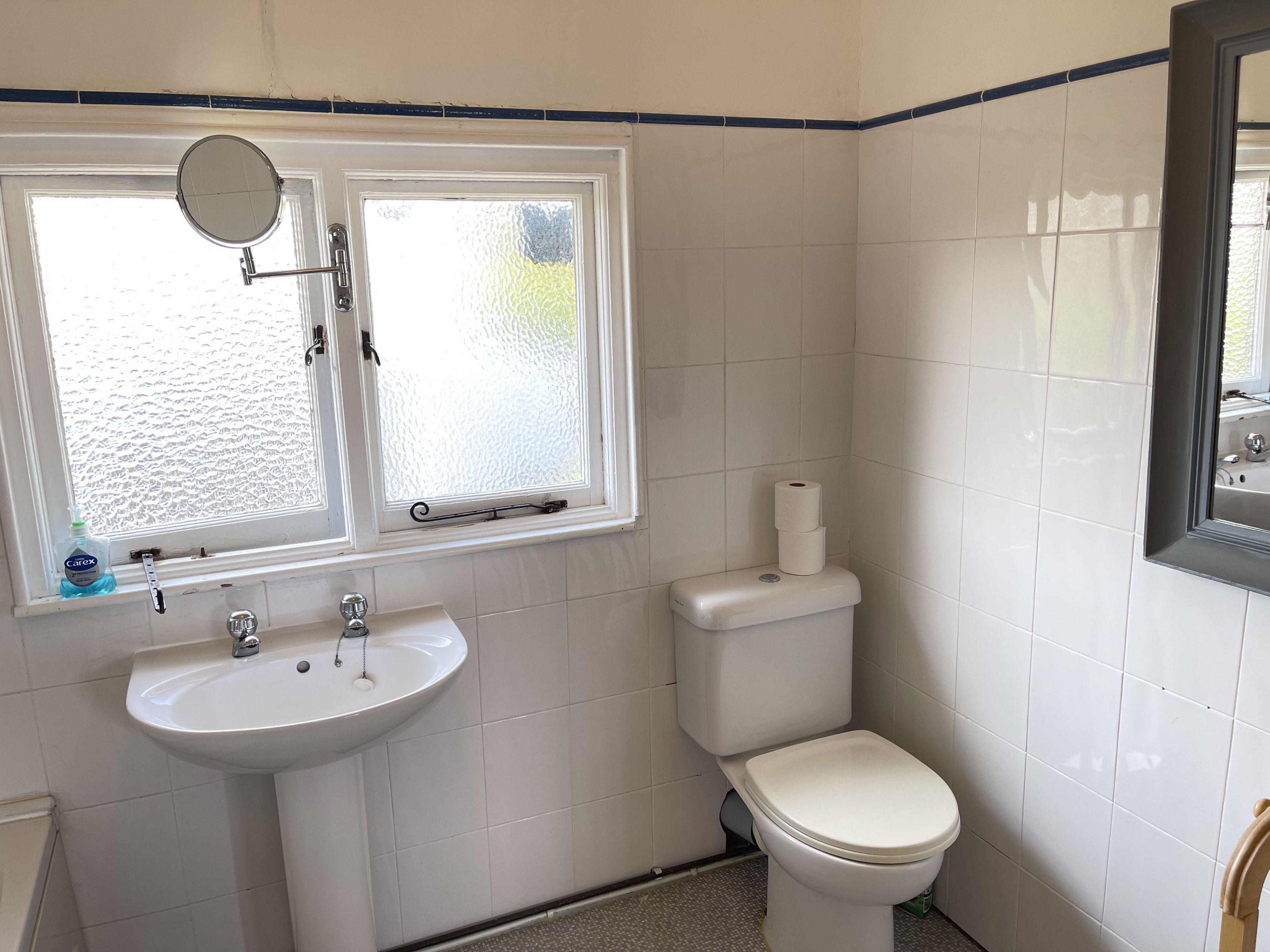 Un bany amb un lavabo blanc, un vàter i una finestra amb mirall.