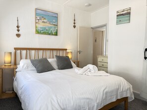 Ein ordentlich bezogenes Bett mit weißen Leinentüchern und zwei Kissen, einer Nachttischlampe und einem gefalteten Handtuch.