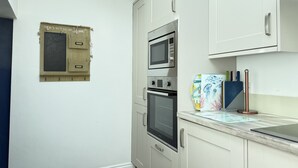 A compact kitchen with white cabinets, a built-in oven, and a microwave. - Treholme - a cottage that sleeps 6 guests in 3 bedrooms (St Ives)