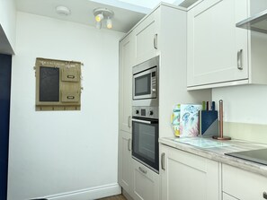 A compact kitchen with white cabinets, a built-in oven, and a microwave. - Treholme - a cottage that sleeps 6 guests in 3 bedrooms (St Ives)