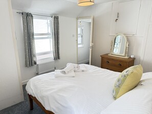 Een hotelkamer met een bed, nachtkastje met spiegel, radiator en raam voorzien van gordijnen.