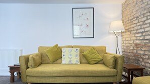 A room with a sofa, a lamp, a framed picture, and a brick wall. - Treholme - a cottage that sleeps 6 guests in 3 bedrooms (St Ives)