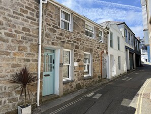 A narrow street with stone buildings, numbered doors, and a potted plant.