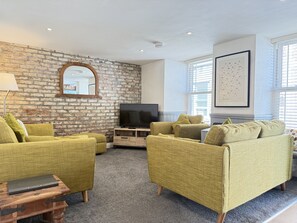 Een woonkamer met een bakstenen muur, een flatscreen televisie en groene banken.