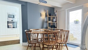 A dining area with a wooden table and chairs, a kitchen with white cabinets and appliances, a blue accent wall, and a sign reading 'CORNWALL'. - Treholme - a cottage that sleeps 6 guests in 3 bedrooms (St Ives)