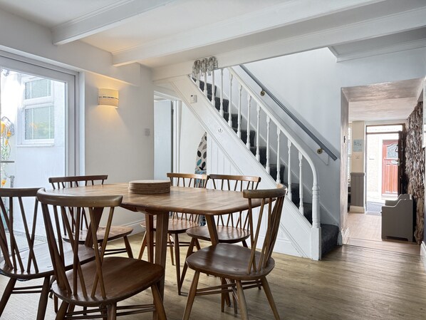 A dining area with a wooden table and chairs, a staircase with white railings, and a view of the outside through a window.