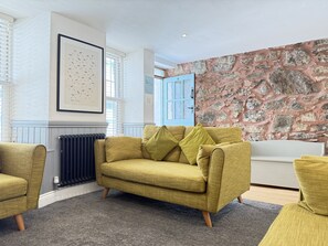 Ein Wohnzimmer mit einem gelben Sofa, einem Heizkörper, einem gerahmten Bild und einer Steinwand.