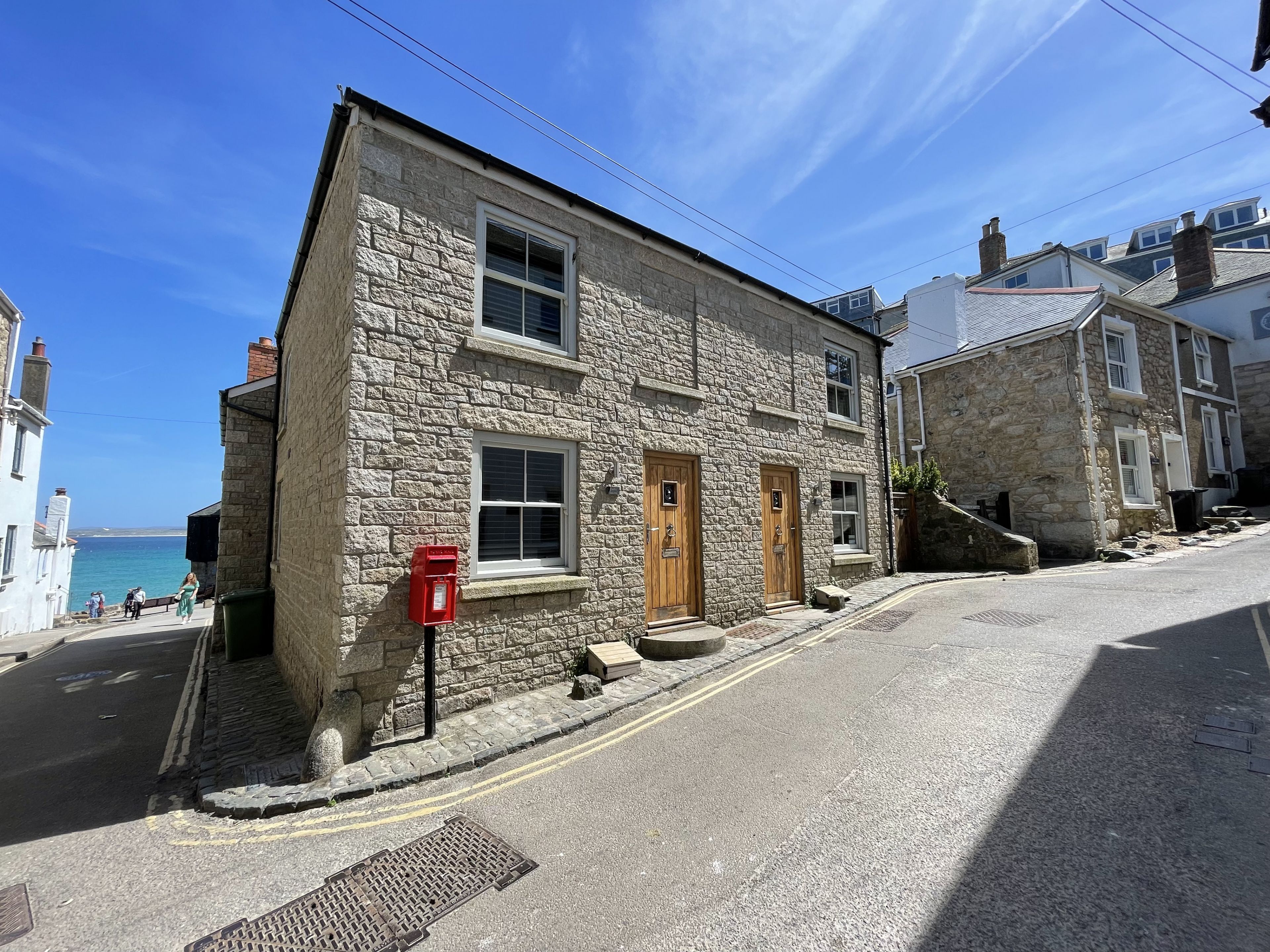 A stone building with a red post box, a small bench, and a clear view of the sea.