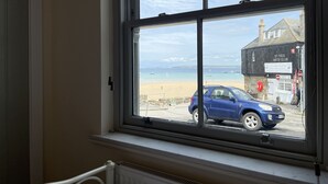 Ein Zimmer mit Fensterblick auf einen Strand, ein abgestelltes Auto und ein Gebäude mit der Aufschrift 'St Ives Arts Club'.