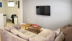 A living room with a sofa set, a coffee table, and a flat-screen TV mounted on the wall. - Harrys Hideout - a cottage that sleeps 4 guests in 2 bedrooms (St Ives)