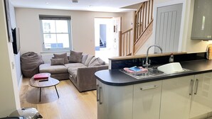A modern kitchen with a built-in island, a seating area with a sofa and a coffee table, and a staircase leading to an upper level. - Harrys Hideout - a cottage that sleeps 4 guests in 2 bedrooms (St Ives)