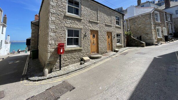 A stone building with a red post box, a small bench, and a clear view of the sea. - Harrys Hideout - a cottage that sleeps 4 guests in 2 bedrooms (St Ives)