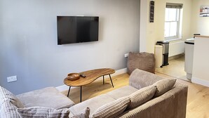 Ein modernes Wohnzimmer mit einem an der Wand befestigten Flachbildfernseher, einem Holztisch und einem beigefarbenen Sofa.