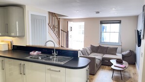 Eine moderne Küche mit integrierter Kücheninsel, ein Essbereich mit Sofa und kleinem Tisch sowie eine Treppe, die zu einer weiteren Ebene führt.