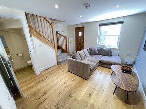 Una sala de estar moderna con una escalera de madera, un sofá modular, una mesita de madera y un ventanal con vistas.