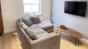 Ein modernes Wohnzimmer mit einer Eckcouch, einem Holztisch und einem flachbildfernseher an der Wand.
